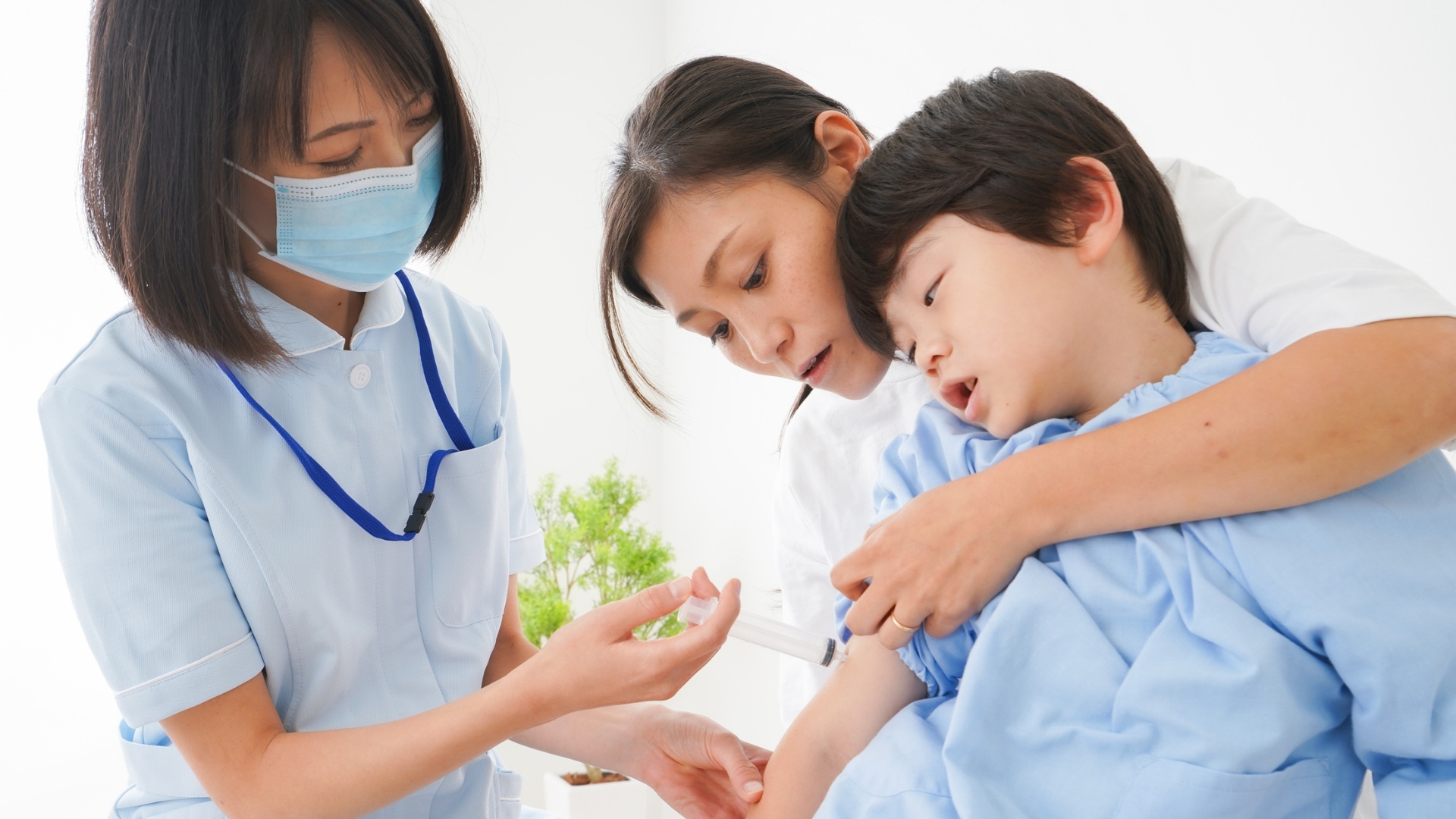 Practice nurse giving a routine childhood immunisation to a smiling toddler on a parent's lap